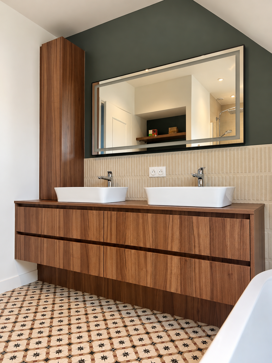 Aménagement d’une salle de bain contemporaine sous combles avec meuble double vasque en bois, miroir lumineux, faïence beige texturée, mur vert profond et carreaux de ciment à motifs.