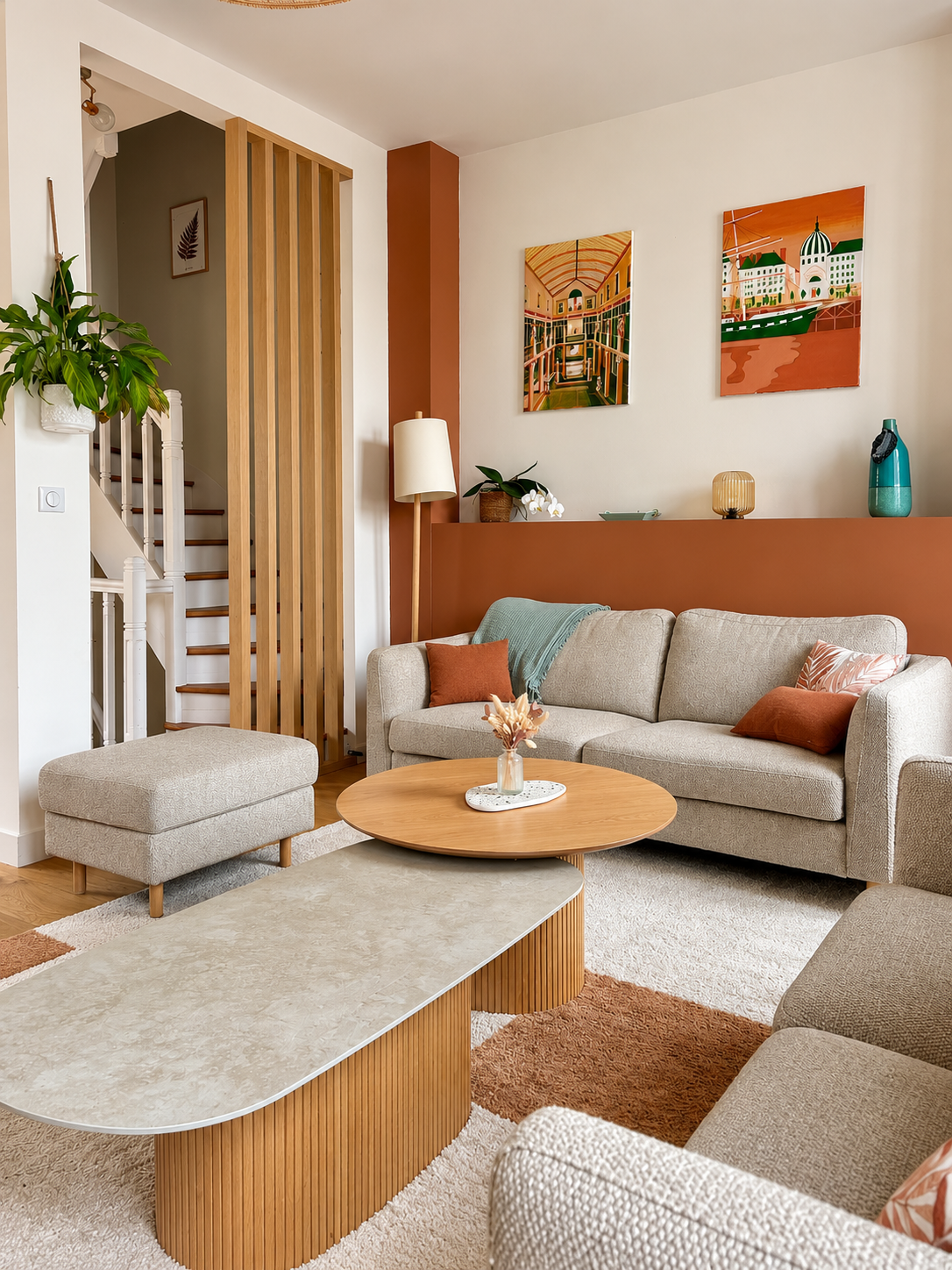 Vue d’un salon lumineux au style scandinave, avec une claustra en bois naturel au premier plan, des canapés en tissu beige, des coussins terracotta, une table basse en bois cannelé et un miroir octogonal au mur.