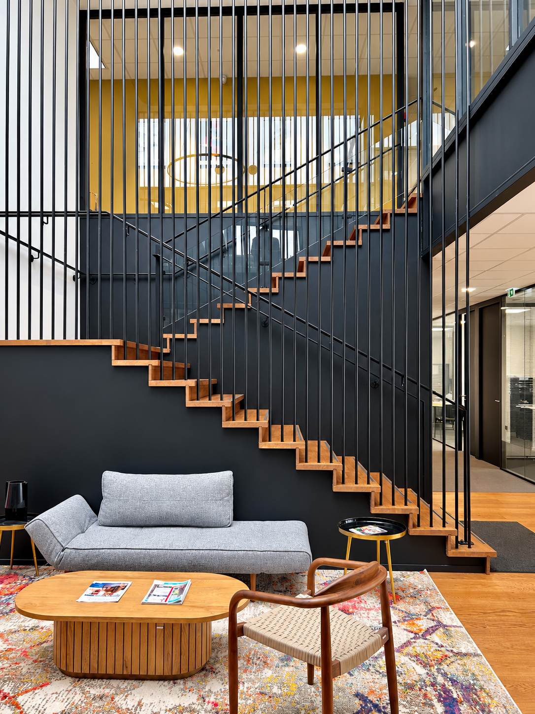 Escalier en bois dans des bureaux contemporains, structuré par des claustras, garde-corps et éléments architecturaux noirs