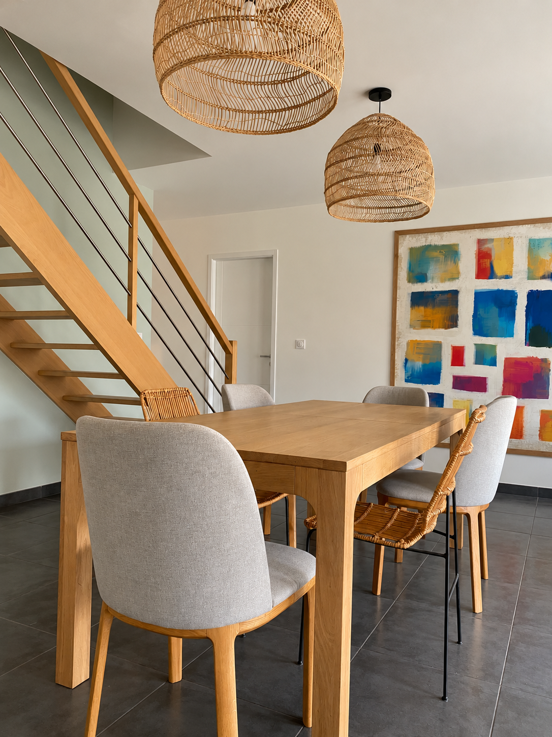 Salon contemporain lumineux et chaleureux, avec canapé aux coussins colorés, mobilier en bois naturel, suspensions en rotin, escalier design, claustra en bois, espace salle à manger convivial et décoration moderne aux accents naturels.