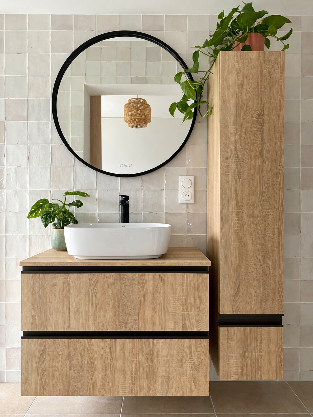 Salle de bain chaleureuse avec meuble vasque en bois, zelliges beige, miroir rond noir et touches végétales